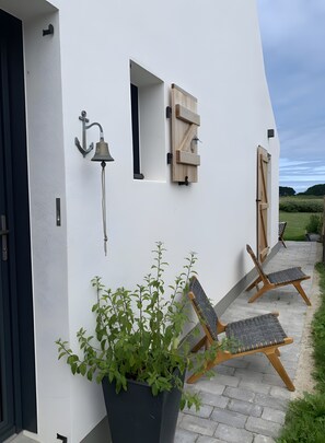 Un bâtiment moderne à l’extérieur blanc, avec une porte noire, un pot de fleurs et deux chevalets en bois.