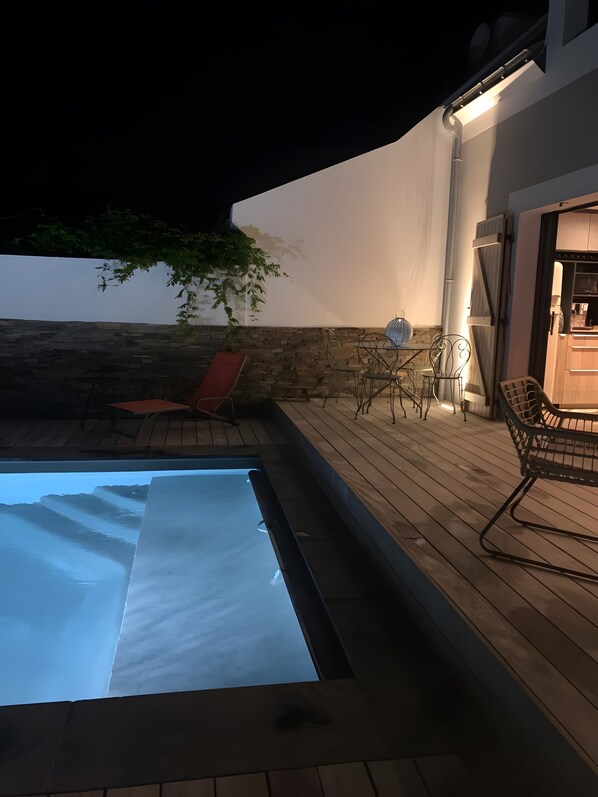 Una piscina con muelle de madera, una silla de descanso roja y una mesa con sillas.