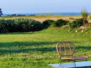 Una silla y una mesa en un área con césped y vista al mar.