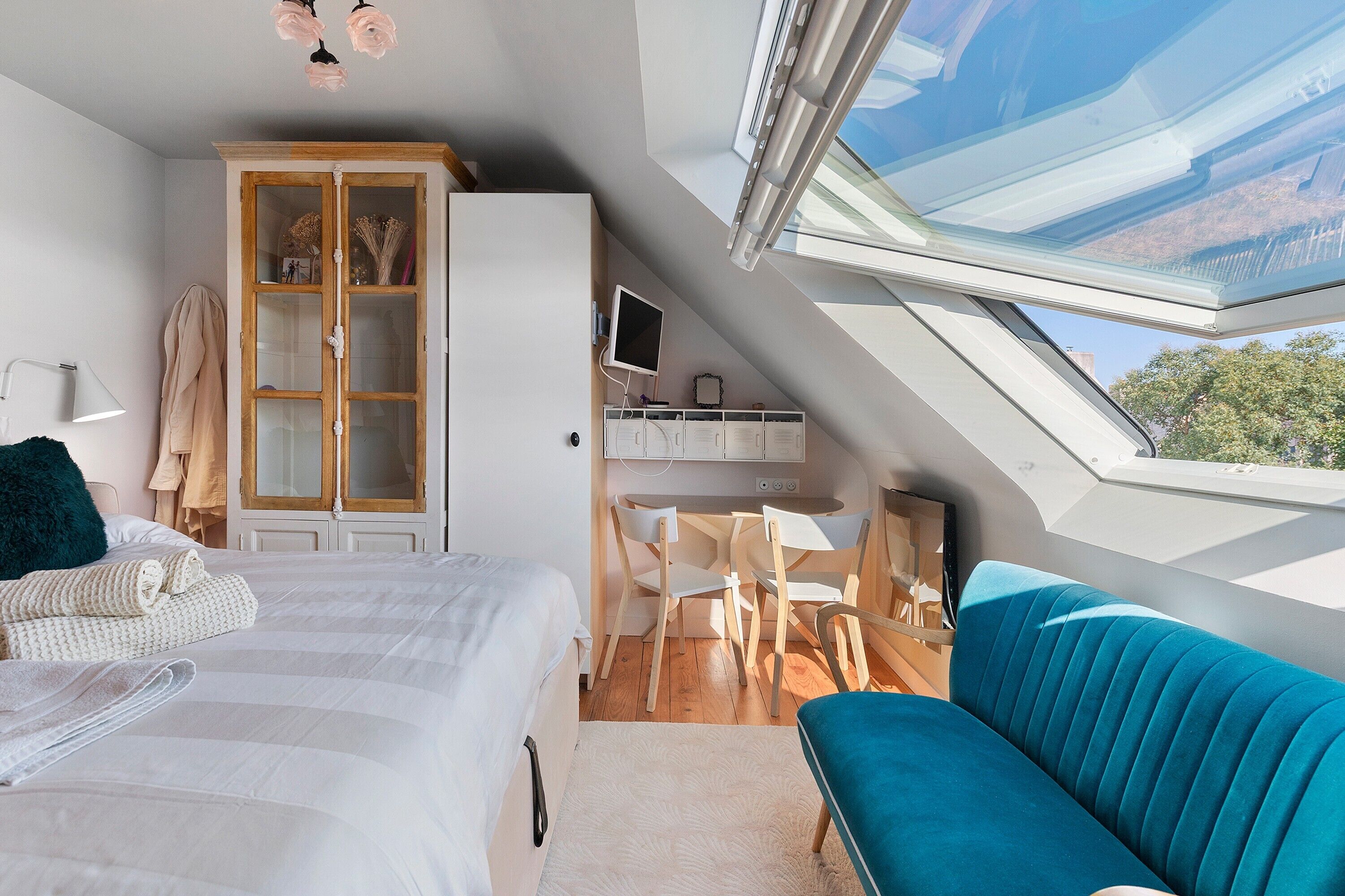 A bedroom with a skylight, a bed, a blue sofa, a wardrobe, and a small kitchenette.