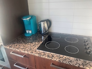 Une cuisine avec un poêle noir, une cafetière bleue et une bouilloire.
