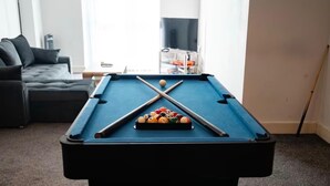 Una mesa de billar con bolas y tacos en una sala de estar con un sofá y una televisión.