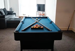 Ein Billardtisch mit Kugeln und Spielstöcken in einem Wohnzimmer mit Sofa und Fernseher.