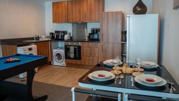 Cocina compacta con armarios de madera, lavadora, microondas y una mesa de comedor para dos personas.