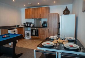 A compact kitchen with wooden cabinets, a washing machine, a microwave, and a dining table set for two. - Apartment Sleeps 7 With Wifi (Birmingham)