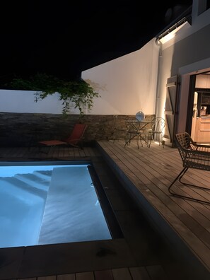 Una piscina con muelle de madera, una silla de descanso roja y una mesa con sillas.
