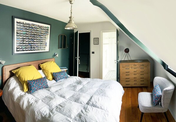Quarto com cama grande, cômoda, cadeira e colagem de fotos na parede.