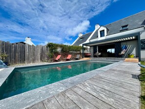 A swimming pool with a wooden deck, a covered patio, and a fenced backyard.