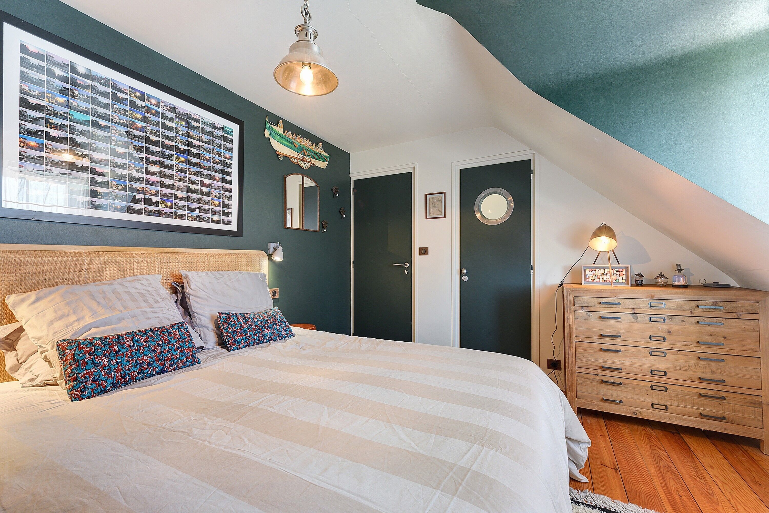A bedroom with a bed, a dresser, a mirror, and a wall-mounted photo collage.