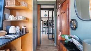 Un pasillo estrecho con estantes de madera, un área de cocina al fondo y una puerta con espejo.