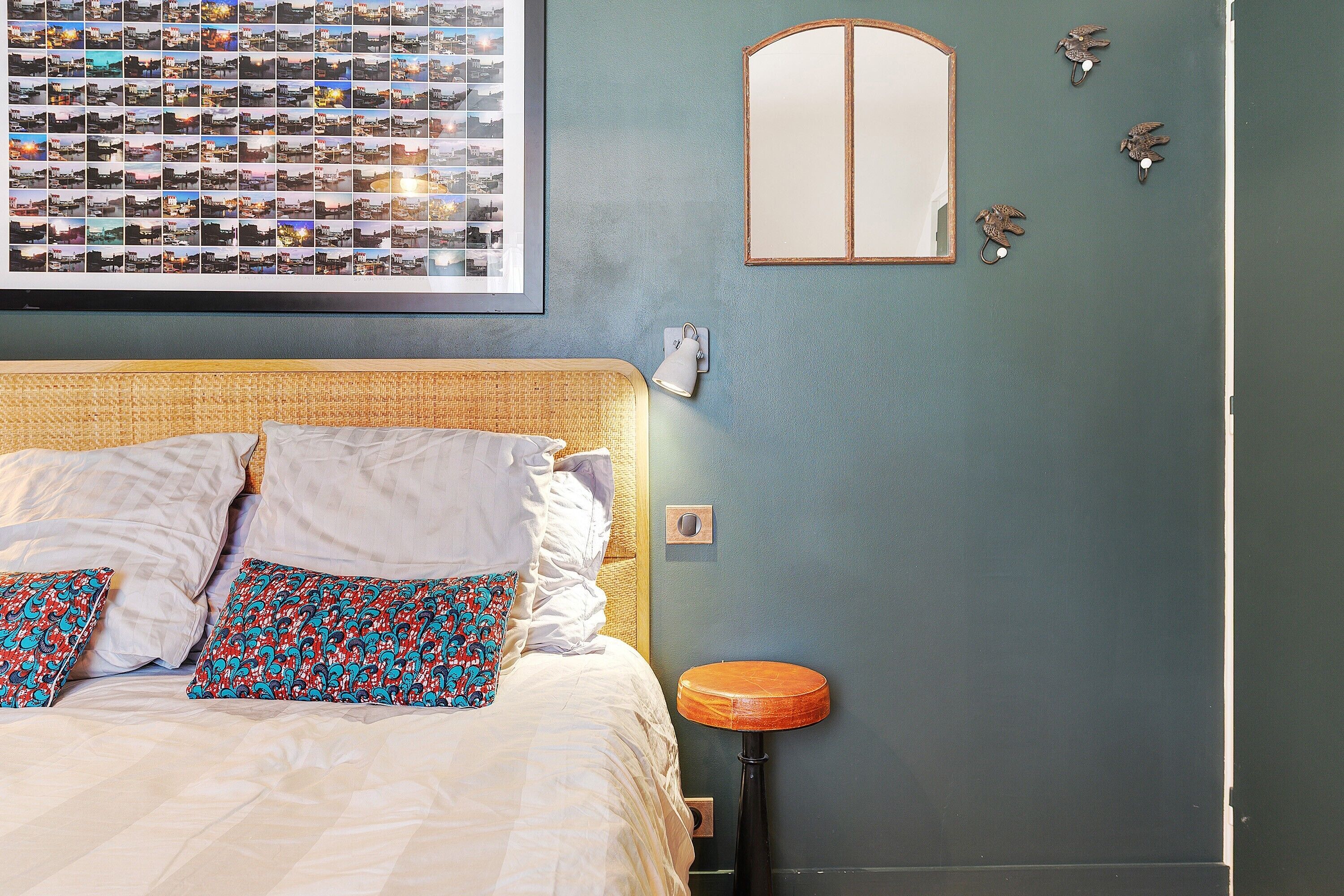 Ein Schlafzimmer mit Bett, Kissen, einer Nachttischlampe, einem wandmontierten Spiegel und einer Fotocollage.