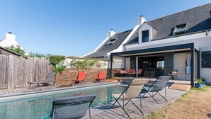Una casa moderna con piscina, mobiliario exterior y un porche cubierto.