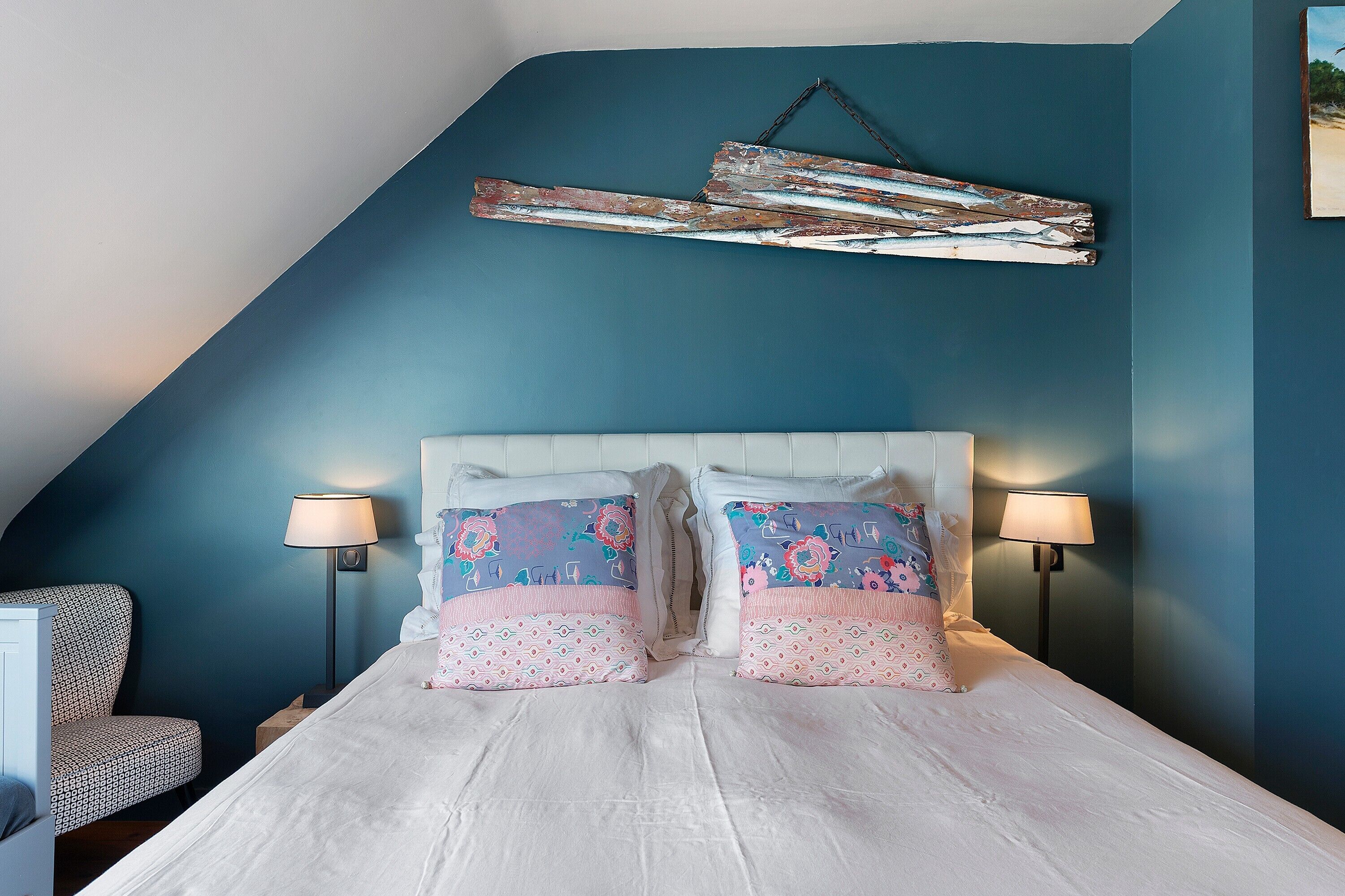 A bedroom with a sloped ceiling, a bed with patterned pillows, two bedside lamps, and a rustic wall decoration.