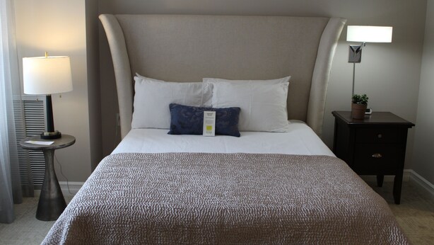A neatly made bed with a textured blanket, two pillows, a bedside lamp, and a small table with a plant. - Cozy Deluxe Queen Room in Minneapolis Boutique Hotel (Minneapolis)