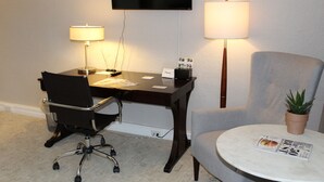 A hotel room with a desk, chair, TV, lamps, and a round table with a magazine. - Cozy Deluxe Queen Room in Minneapolis Boutique Hotel (Minneapolis)