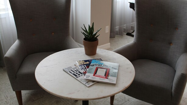 Une pièce comprenant deux fauteuils, une petite table avec des magazines et une plante en pot.