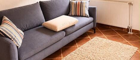 A living room with a sofa, pillows, a rug, a radiator, and a window with curtains.