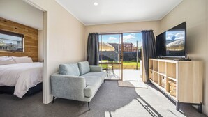 Une chambre d’hôtel moderne équipée d’un lit, d’un canapé, d’une télévision et d’une porte-fenêtre coulissante donnant sur l’extérieur.