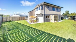 Une maison moderne à deux étages, dotée d’une pelouse bien entretenue et de meubles de jardin.