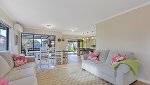 A living room with a sofa, a dining table, and chairs. There is a kitchen area in the background. - Roy-Al Retreat - Riwaka Holiday Home (Riwaka)