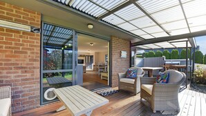 A covered outdoor area with a wooden deck, wicker furniture, and a glass door leading to an interior space. - Roy-Al Retreat - Riwaka Holiday Home (Riwaka)