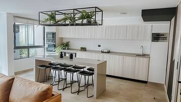 A modern kitchen with a central island, bar stools, and a hanging plant.