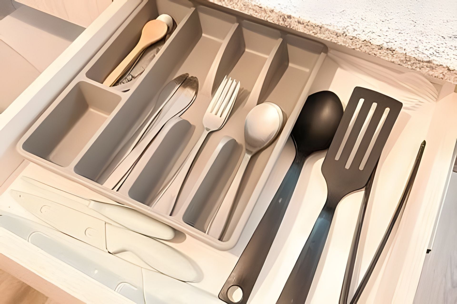 A drawer with compartments containing various kitchen utensils.