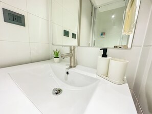 A bathroom with a white sink, a mirror, a potted plant, and two white dispensers. - Moderno depto. en Stgo. cerca del metro (Santiago)