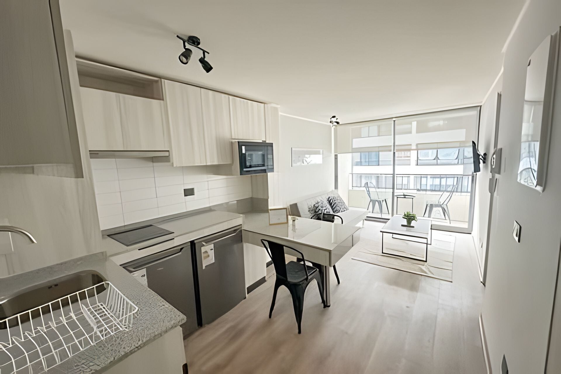 Una cocina moderna con armarios blancos, un comedor con mesa y sillas, y un amplio ventanal con vistas al exterior.