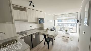 Una cocina moderna con armarios blancos, un comedor con mesa y sillas, y un amplio ventanal con vistas al exterior.