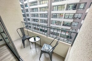 A balcony with a glass door, two chairs, a small round table, and a potted plant. - Moderno depto. en Stgo. cerca del metro (Santiago)