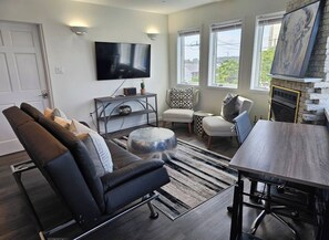 Ein modernes Wohnzimmer mit Sofa, Ohrensessel, Hocker und Esstisch.