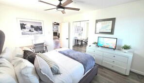 Ein Schlafzimmer mit Bett, Schreibtisch, Fernseher und Deckenventilator.