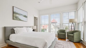 A bedroom with a large bed, two armchairs, a floor lamp, and a view of buildings through large windows. - The Coral Steps to King and Michelin Restaurants (Charleston)