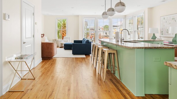 A modern kitchen with a green island, wooden bar stools, and a blue sofa in the living area. - The Coral Steps to King and Michelin Restaurants (Charleston)
