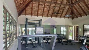 A gym with exercise equipment, a ceiling with wooden beams, and a large mirror. - Pool View Apartment at 'Domaine dès Alizées Club & Spa' (Grand Baie)
