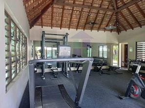 A gym with exercise equipment, a ceiling with wooden beams, and a large mirror. - Pool View Apartment at 'Domaine dès Alizées Club & Spa' (Grand Baie)