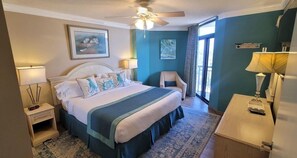 Ein Hotelzimmer mit Bett, Sessel, Schreibtisch, Deckenventilator und Bildern an den Wänden.