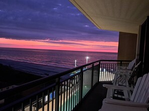 Ein Balkon mit Blick auf den Ozean bei Sonnenuntergang, mit Geländer und einigen Stühlen.