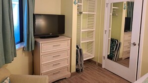 Ett rum med en tv-apparat på en byrå, en garderob med vita hyllor och en dörr med en spegel.