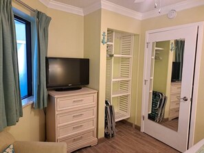Ein Zimmer mit einem Fernseher auf einer Kommode, einem Schrank mit weißen Regalen und einer Tür mit einem Spiegel.