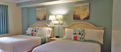 A hotel room with two beds, a ceiling fan, wall art, and a nightstand with a lamp.