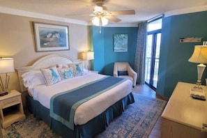 Ein Hotelzimmer mit einem Bett, einem Sessel, einem Schreibtisch, einem Deckenventilator und Bildern an den Wänden.