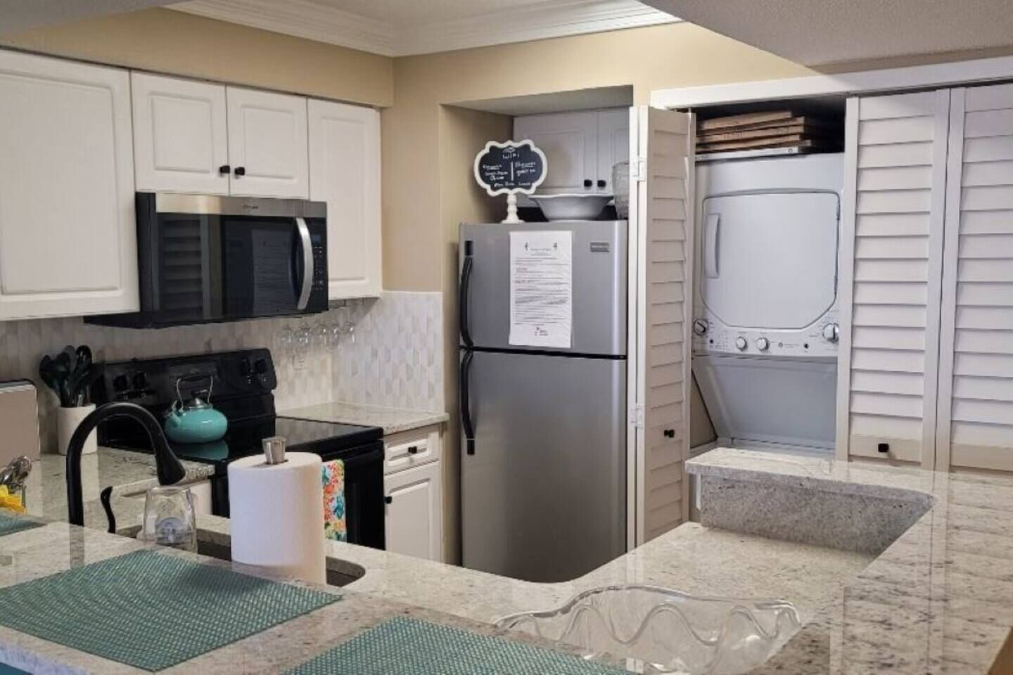 A kitchen with white cabinets, a stainless steel refrigerator, a microwave, and a sink with a granite countertop.