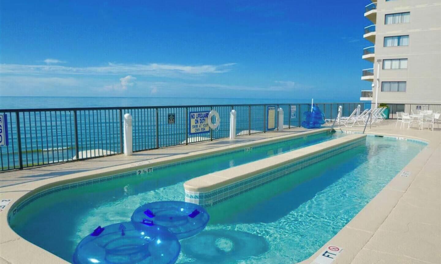 A swimming pool with a view of the ocean, a lifeguard sign, and lounge chairs.