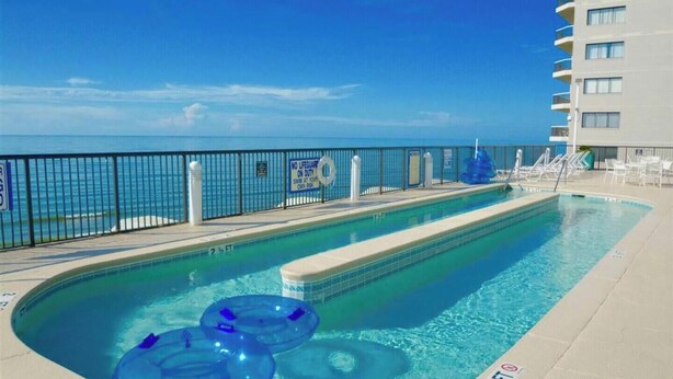 En pool med utsikt över havet, en skylt med information om badvakten och solstolar.