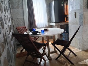 Un coin repas avec une table ronde, deux chaises en bois, un bol noir, un verre bleu et une bouteille d’eau.