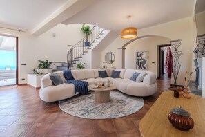 Un salon spacieux avec un grand canapé en forme de L, une table basse ronde et un escalier agrémenté d’une plante.