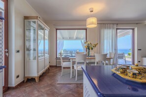 Une pièce comprenant un coin repas, une vue sur la mer, un meuble avec des portes en verre et un luminaire au plafond.