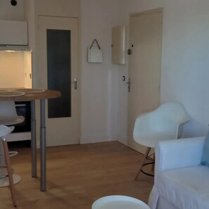 A room with a dining table, a white chair, a sofa, and a cabinet. - Feet in the water (Palavas-les-Flots)